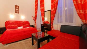 A bedroom with a red bed, a black sofa, a glass coffee table, and a mirror.