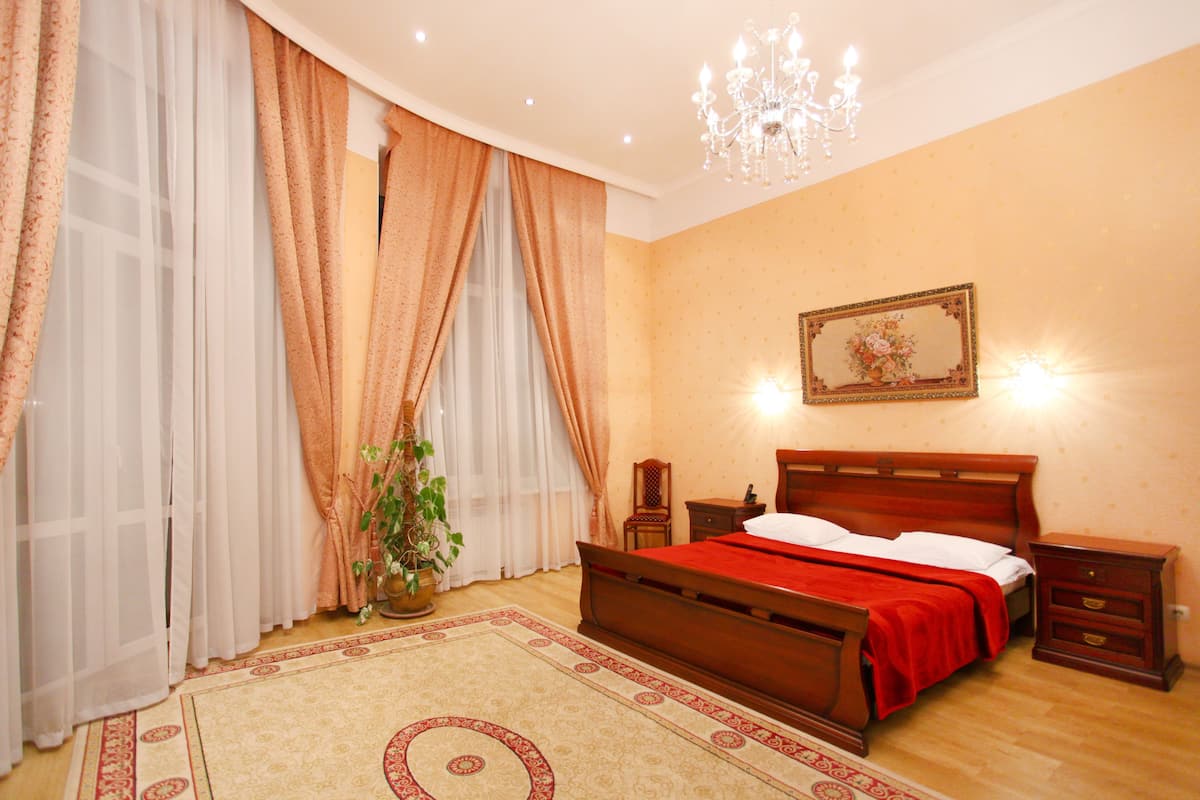 A bedroom with a wooden bed, a nightstand, a bedside table, a chandelier, and a potted plant.