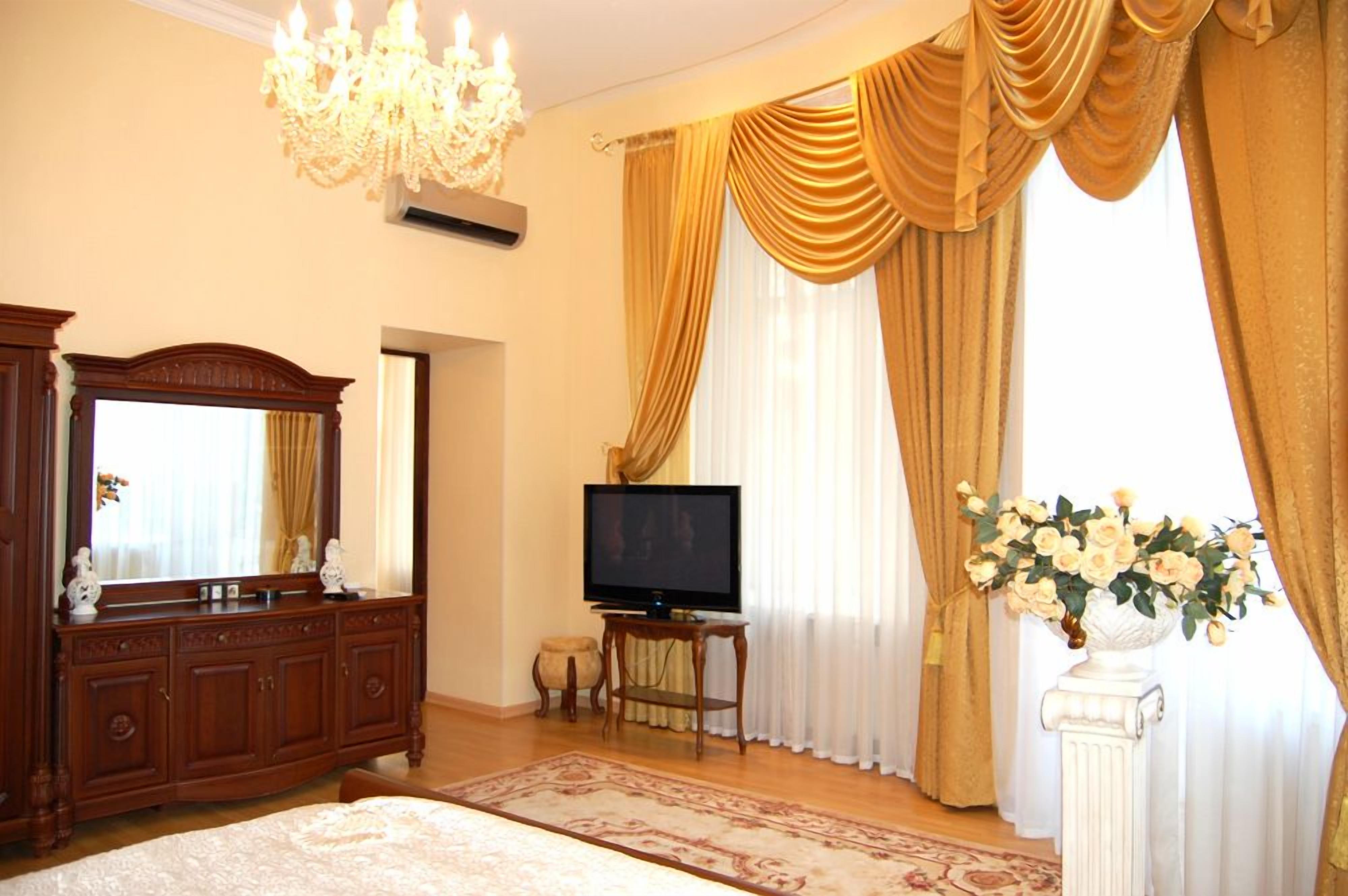 A room with a large mirror, a television on a stand, a decorative vase with flowers, and a chandelier.