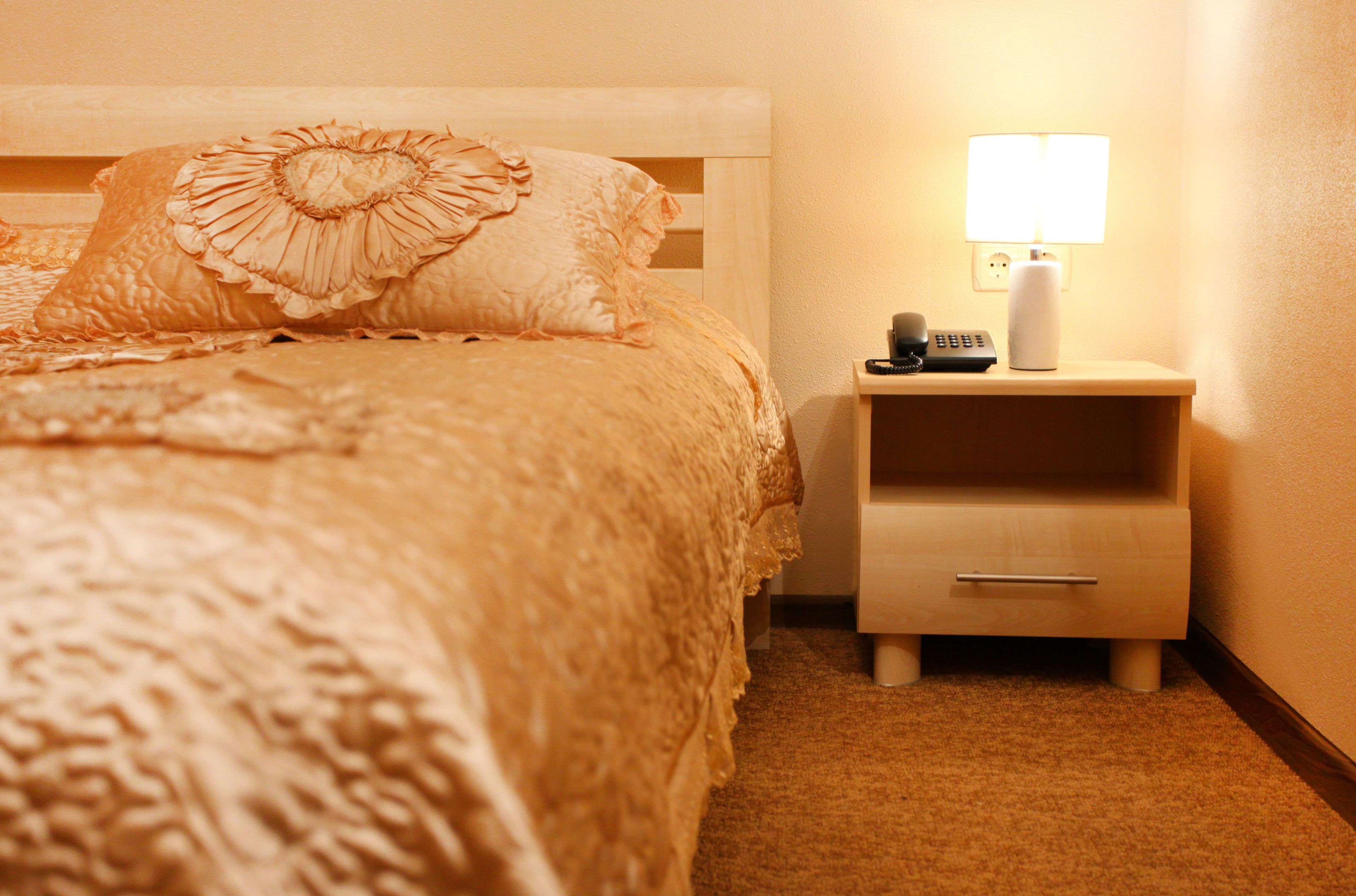 A neatly made bed with a decorative pillow, a bedside table with a lamp, and a drawer.