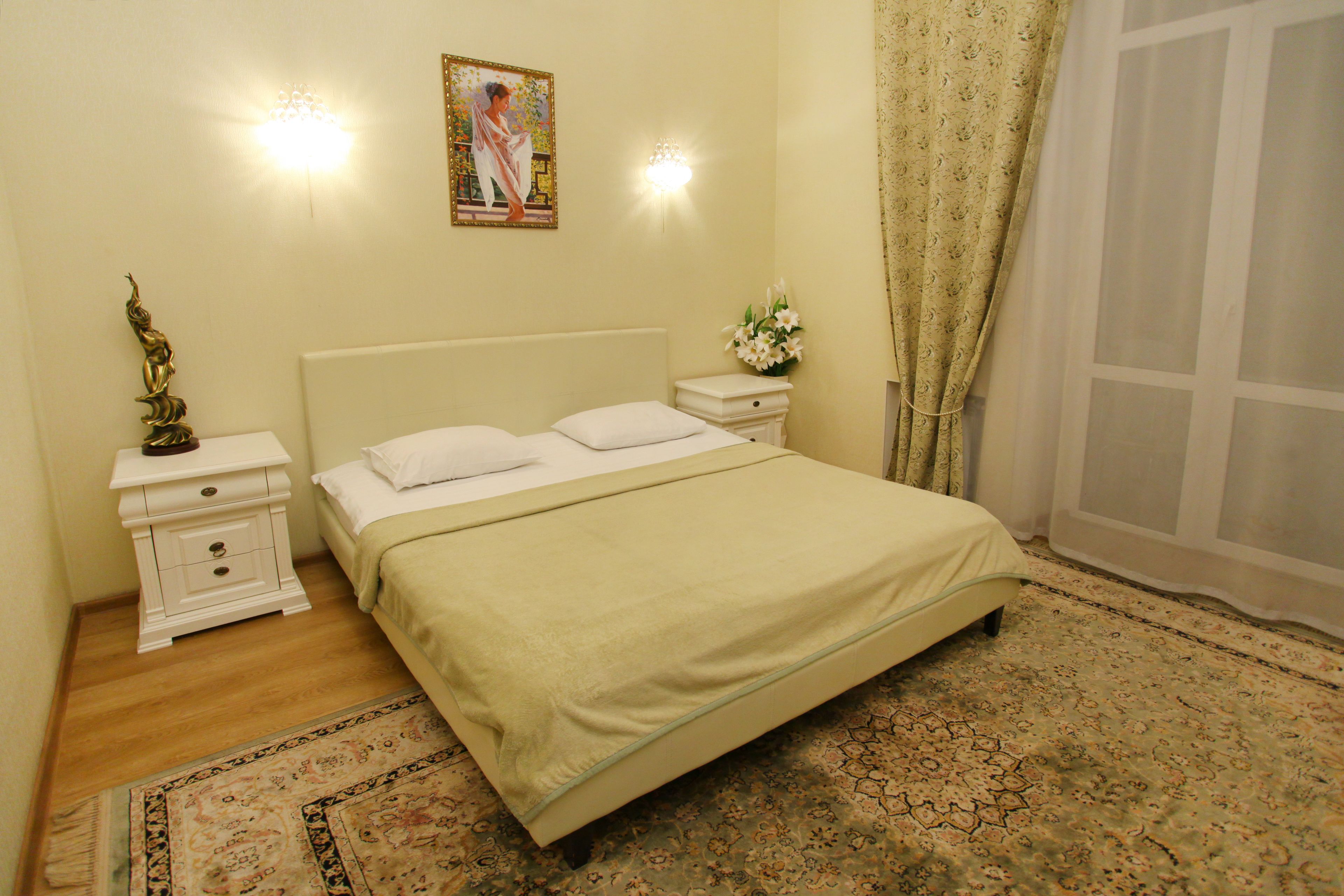 Una cama bien hecha con sábanas blancas, una mesita de noche con una lámpara y un arreglo floral.