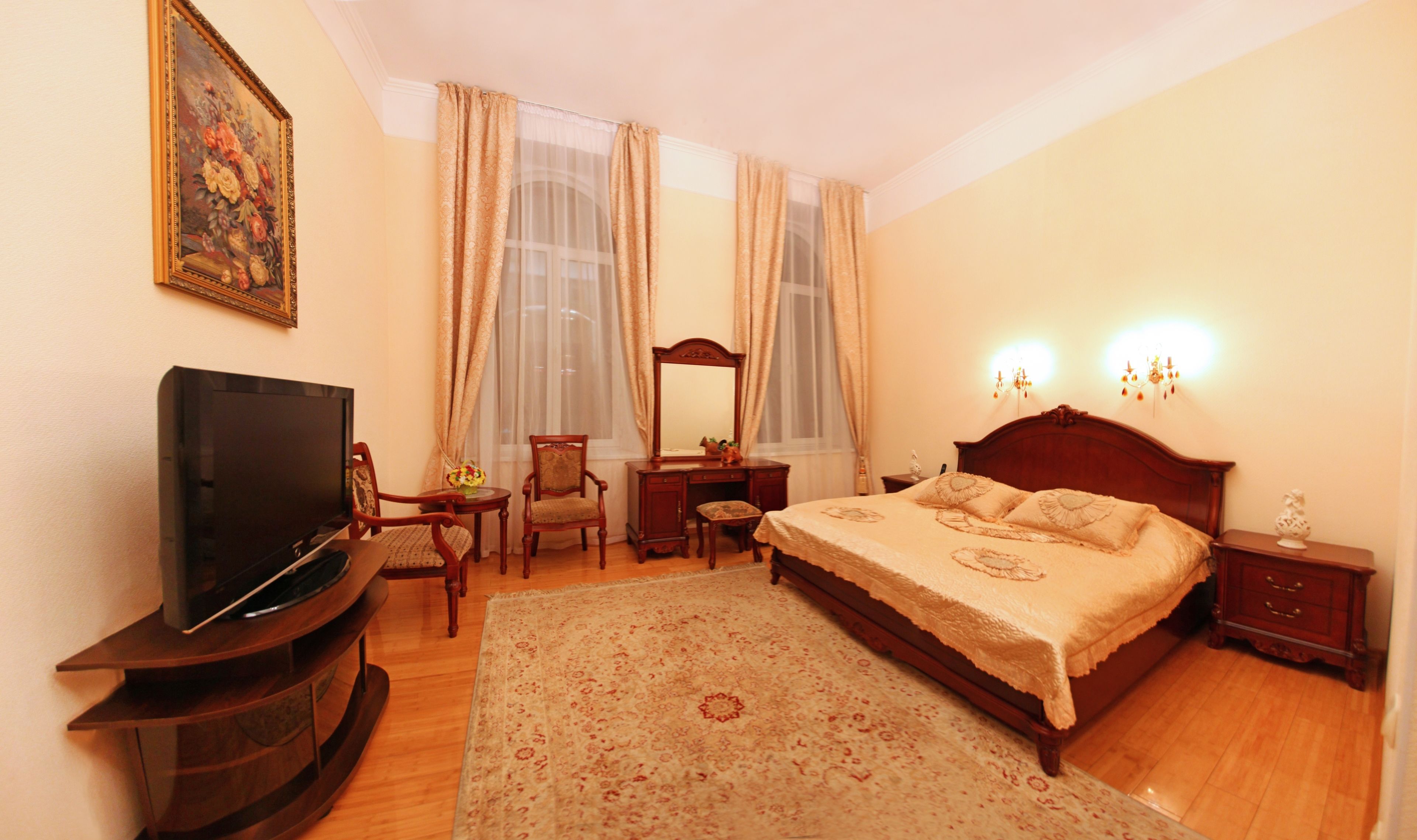 A bedroom with a bed, a TV, a desk, a chair, a dresser, and a mirror.