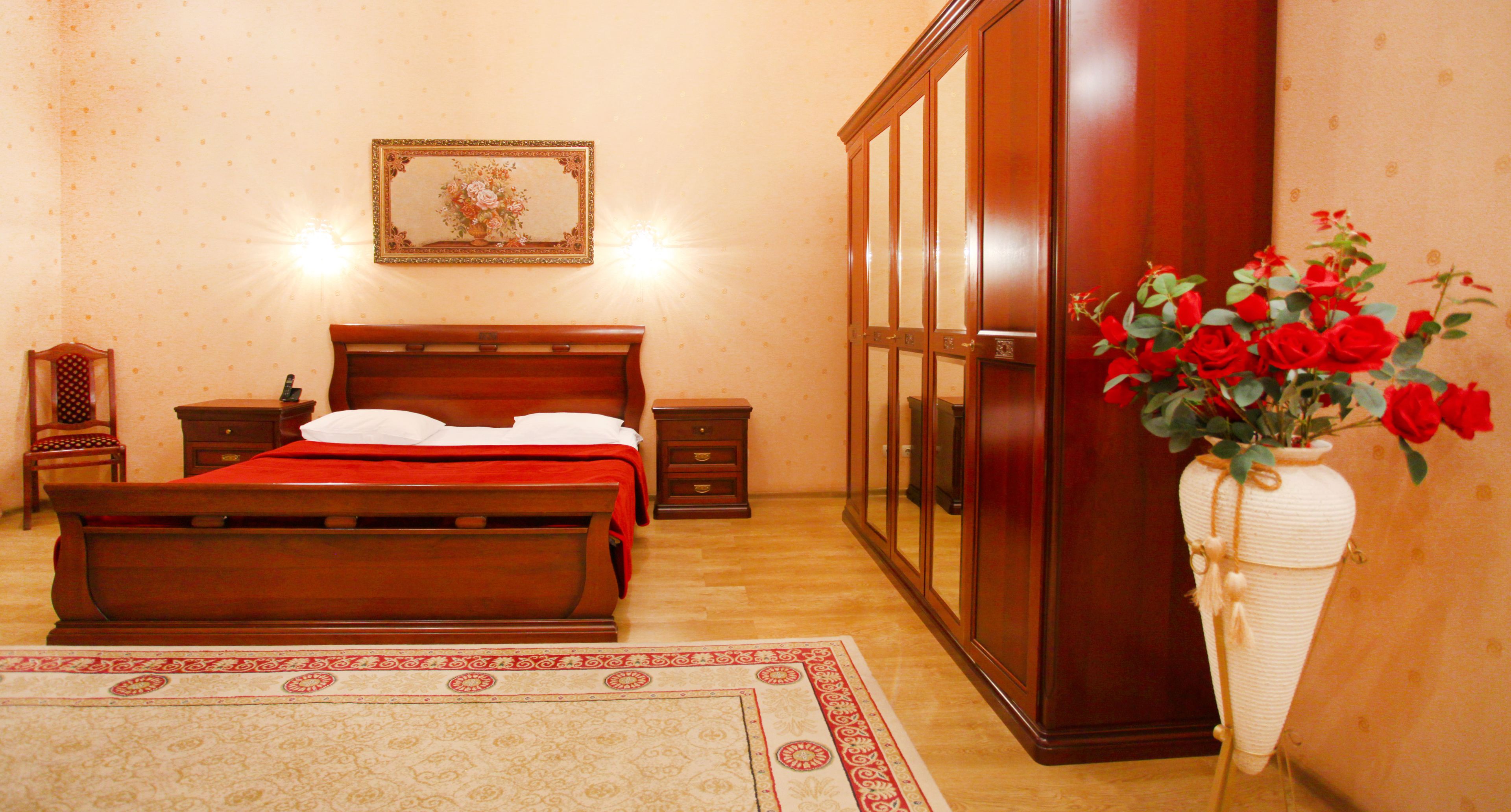Un dormitorio con una cama de madera, una mesita de noche, un aparador y un jarrón de rosas rojas.