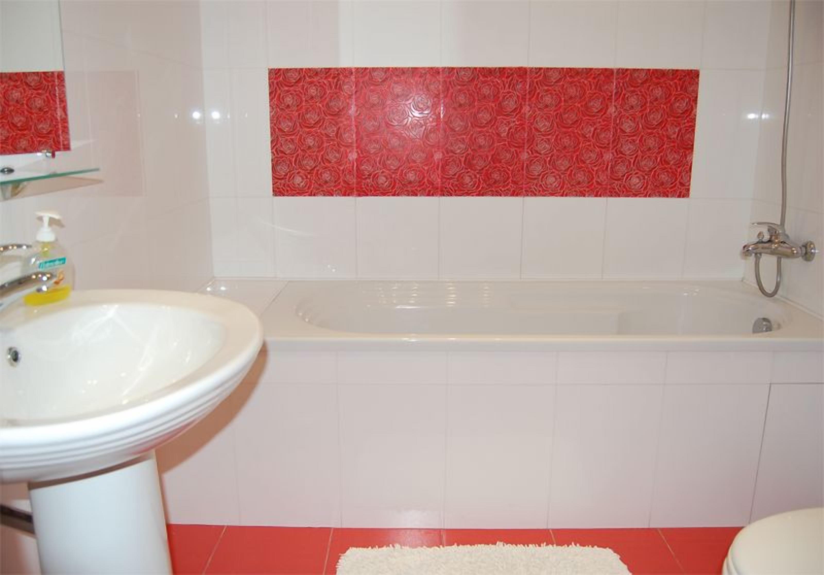 Un baño con un lavabo blanco, una bañera y baldosas rojas con diseño en la pared.