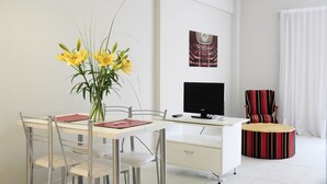 A modern living room with a dining table, chairs, a TV, and a striped armchair. - Apart Via 51 (La Plata)