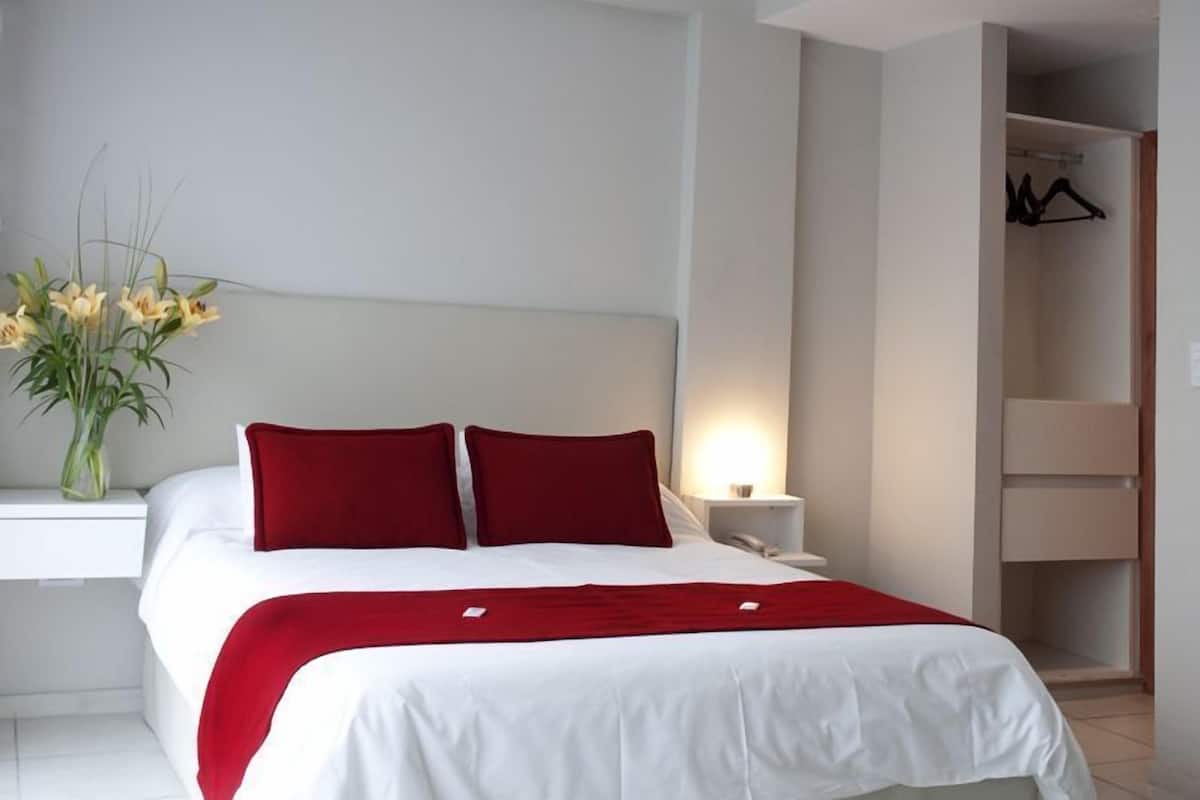 A neatly made bed with white and red bedding, a bedside table with a lamp, and a vase with flowers.