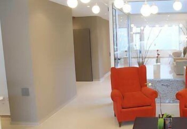 Een moderne woonkamer met een glazen scheidingswand, een rode fauteuil en een salontafel.