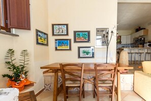 A dining area with a wooden table and chairs, surrounded by framed artwork on the wall.