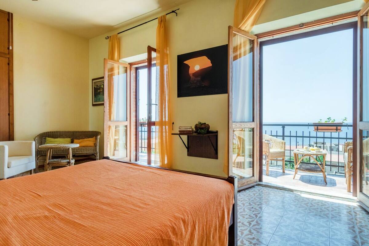 A hotel room with a large bed, a sofa, a small table, and a balcony with a view.