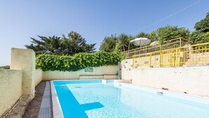 An outdoor swimming pool with a clear blue water surface, surrounded by a stone wall and a yellow fence. - Mare Lughente (Cuglieri)