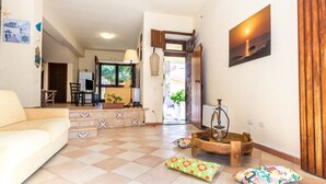 A spacious living area with a sofa, a coffee table, and a fireplace. There is a door leading to another room and a view of the outdoors. - Mare Lughente (Cuglieri)