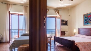 A room with two beds, a balcony, a wicker chair, and a painting on the wall. - Mare Lughente (Cuglieri)