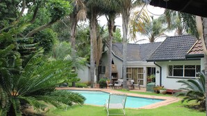 Une maison avec une piscine, entourée d’une végétation luxuriante et de palmiers.