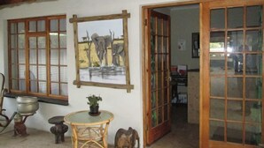 Une pièce avec un plafond en bois, un tableau représentant des éléphants, une table ronde entourée de chaises et une porte donnant sur une autre pièce.