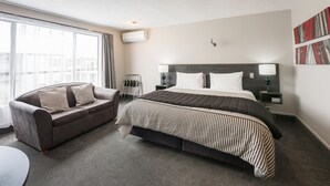 A modern hotel room with a large bed, a sofa, a bedside table, and a window with curtains. - Strathern Motor Lodge (Christchurch)