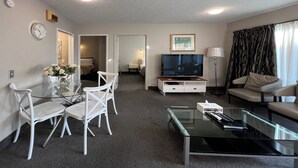 A modern living room with a glass coffee table, white chairs, a TV, and a sofa. - Strathern Motor Lodge (Christchurch)