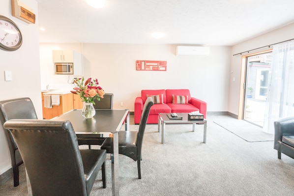 A modern living room with a red sofa, a dining table with chairs, and a kitchen area in the background.
