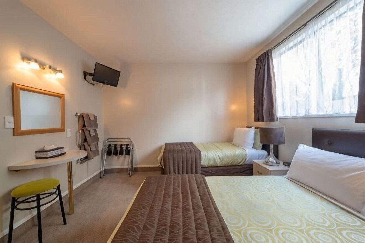 A hotel room with a bed, a desk, a chair, a TV, and a window with curtains.