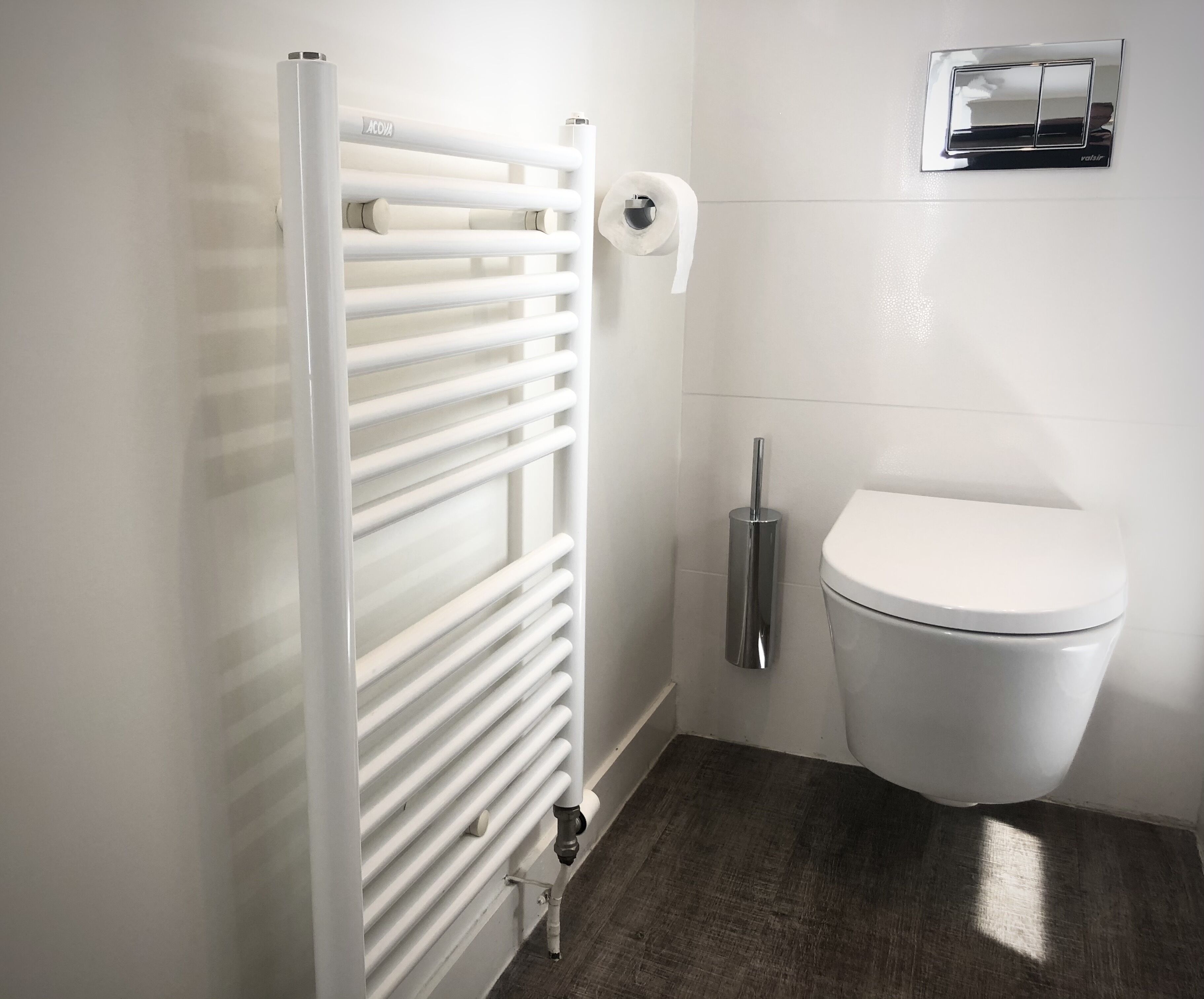 A bathroom with a white radiator, a toilet, and a hand dryer.