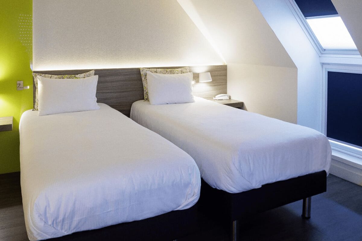 A twin room with two beds, a skylight, a nightstand with a lamp, and a green accent wall.