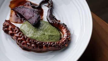 A white plate with octopus, green sauce, and brown sauce on a wooden table.