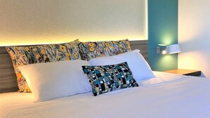 A neatly made bed with white linens and two decorative pillows, one with a floral pattern and another with a geometric design. - Logis Hôtel & Restaurant Les Mouettes - Larmor Plage, proche de Lorient (Larmor-Plage)