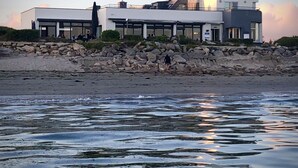 A modern coastal building with a stone retaining wall and a beach in the foreground. - Logis Hôtel & Restaurant Les Mouettes - Larmor Plage, proche de Lorient (Larmor-Plage)