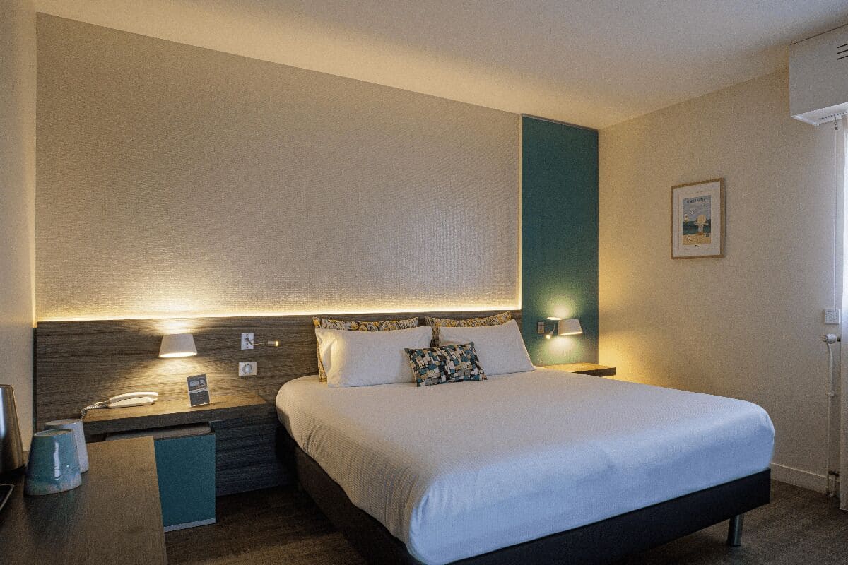 A hotel room with a bed, bedside tables, a lamp, a telephone, and a picture on the wall.