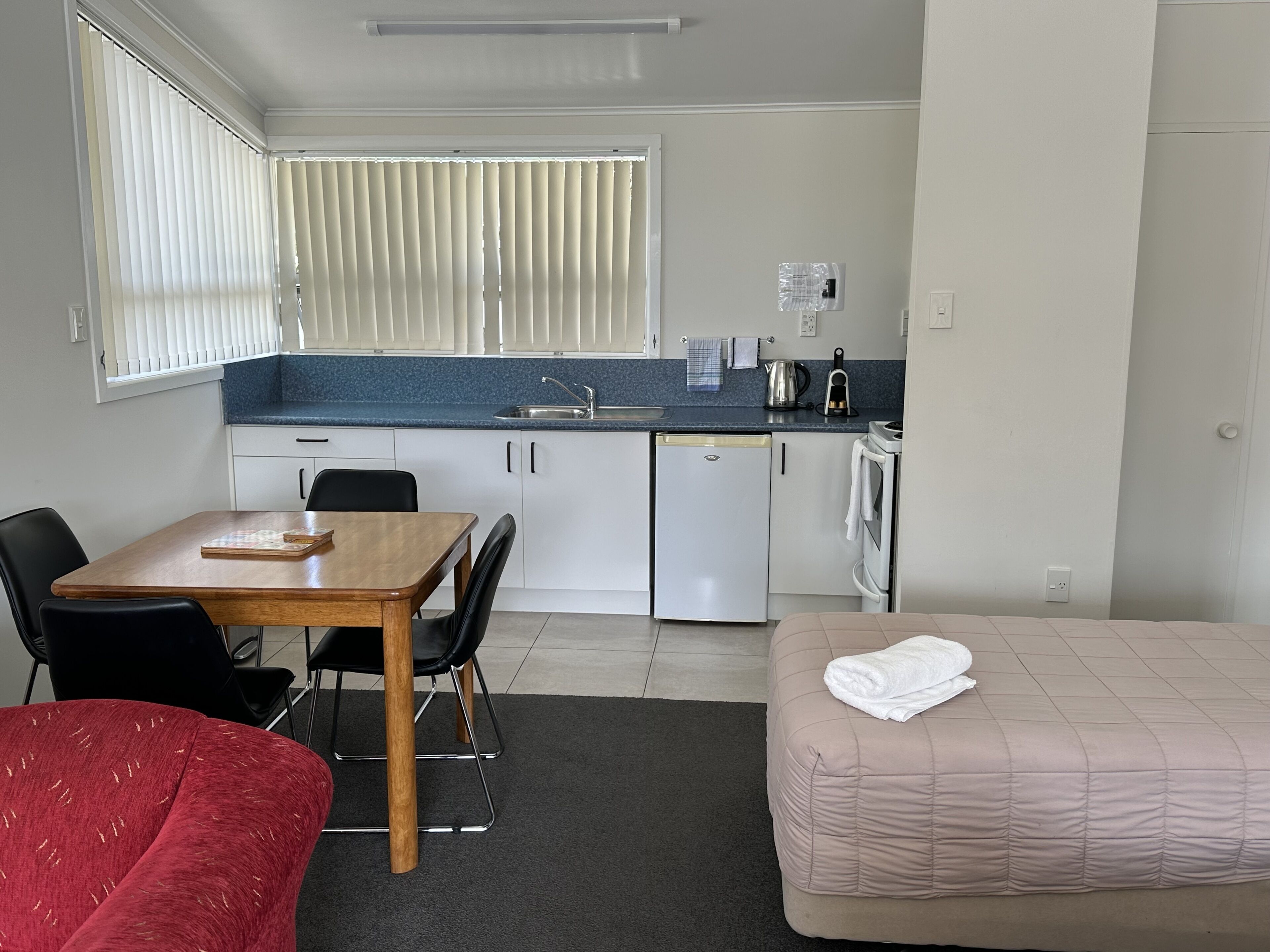 Una habitación de hotel compacta con kitchenette, comedor y cama.