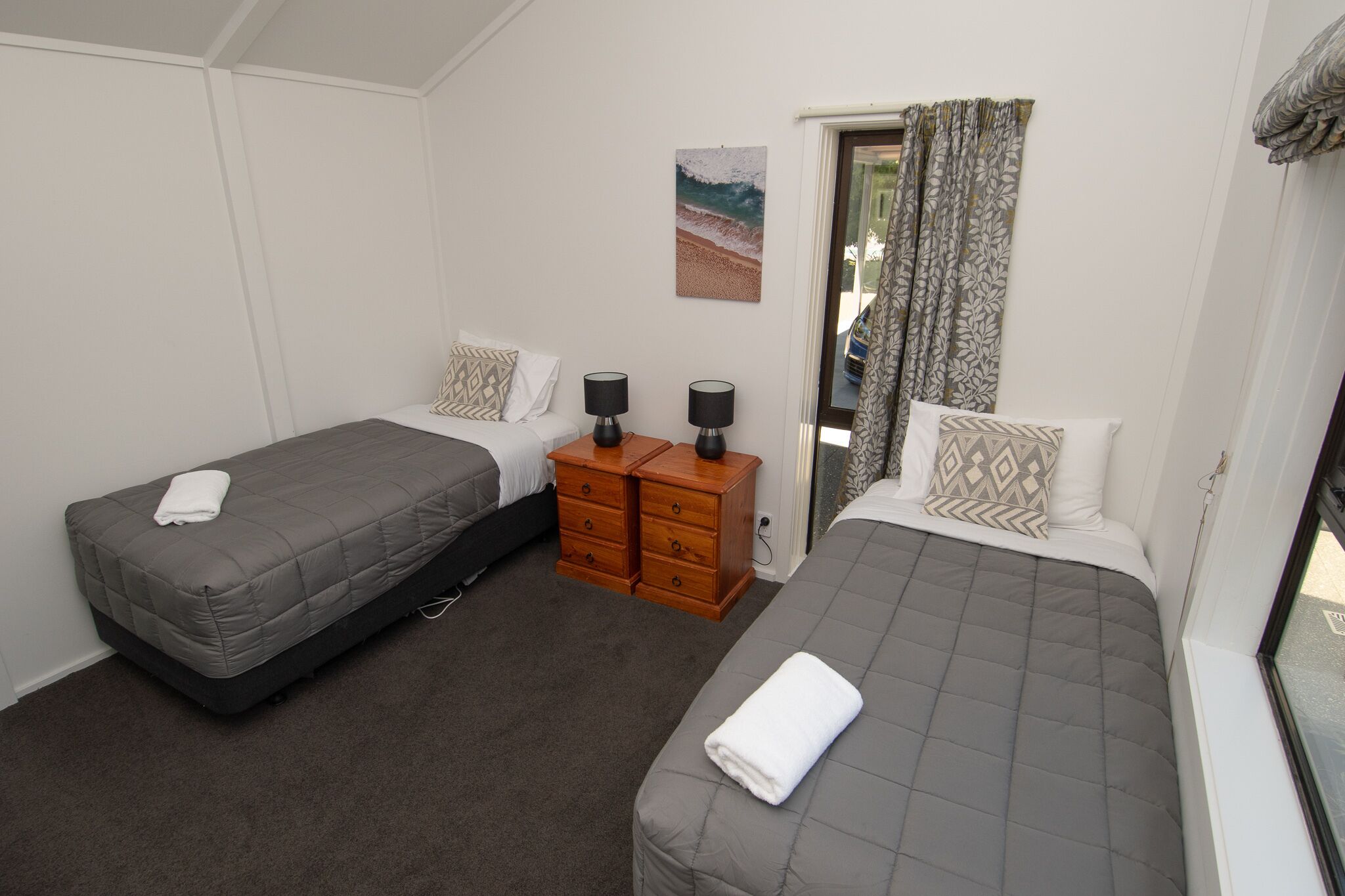 A bedroom with two beds, a wooden dresser, and a window with curtains.