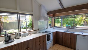 A kitchen with a stove, oven, and sink, wooden cabinets, and large windows with a view of greenery. - Middle Park Motel (Blenheim)