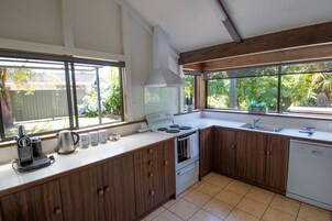 Cocina con estufa, horno y lavaplatos, armarios de madera y ventanas amplias con vistas a la vegetación.
