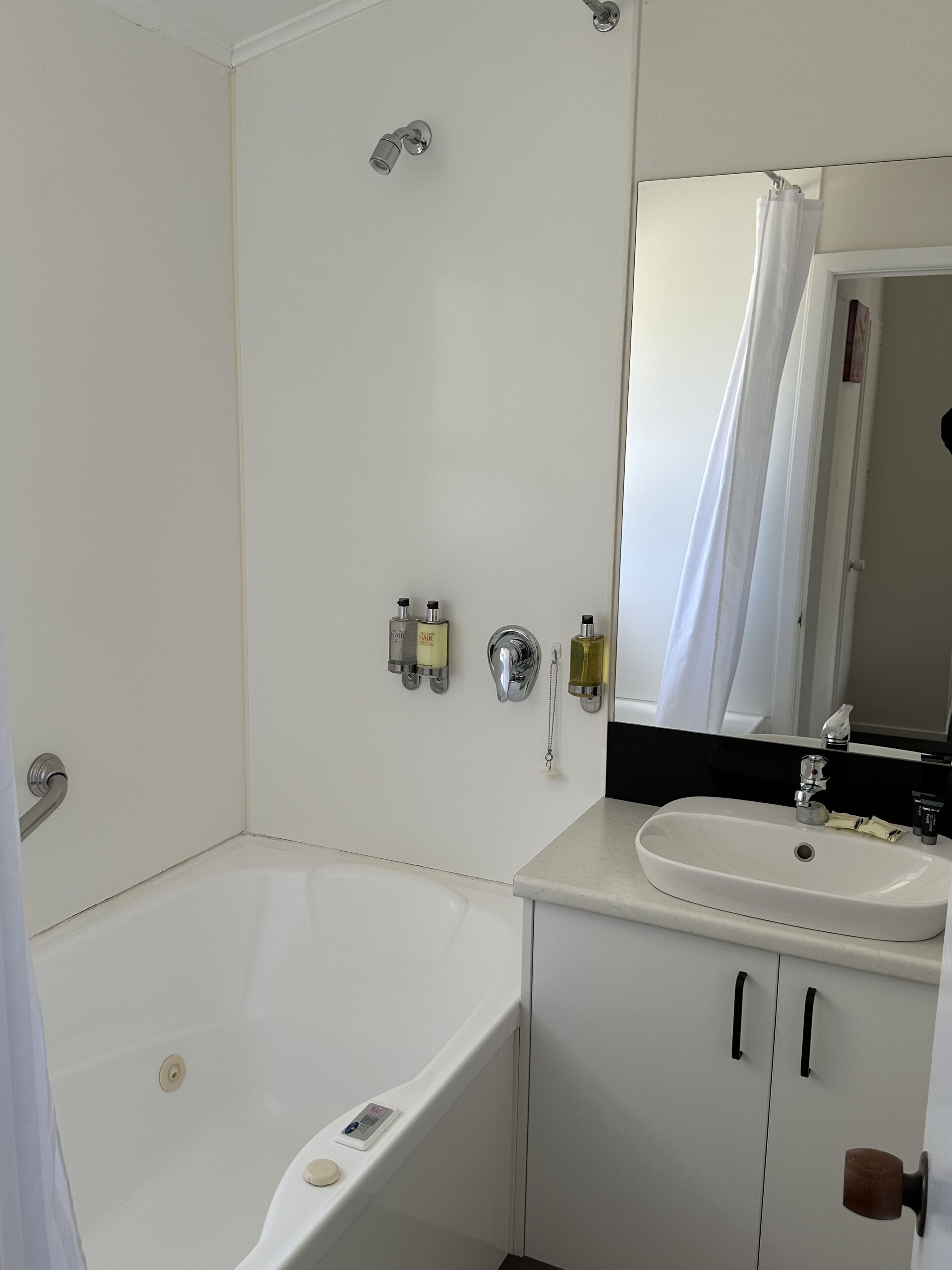 Een badkamer met een bad, een wastafel en een spiegel. Er staan toiletartikelen aan de wand en er is een douchegordijn.