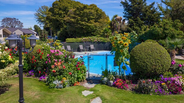 A swimming pool surrounded by colorful flowers and a well-maintained lawn. - Middle Park Motel (Blenheim)