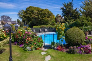 Una piscina rodeada de flores coloridas y un césped bien cuidado.