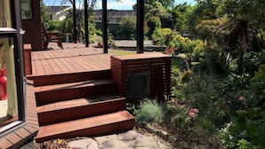 A wooden deck with steps leading to a covered area, surrounded by lush greenery and a variety of plants. - Middle Park Motel (Blenheim)