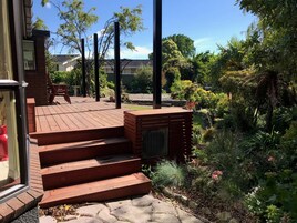 Una terraza de madera con escalones que conducen a una zona cubierta, rodeada de abundante vegetación y diversas plantas.