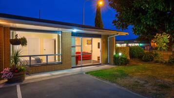 A modern house with a large glass door leading to a living area, a visible red couch, and a well-lit street lamp.