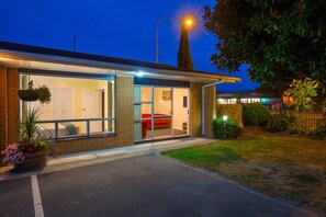 Una casa moderna con un amplio ventanal que da a una sala de estar, un sofá rojo visible y un poste de luz iluminado.