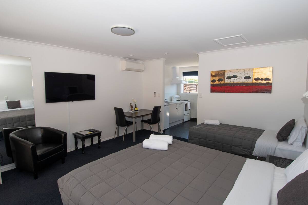 A hotel room with a large bed, a desk with two chairs, a TV mounted on the wall, and a painting above the bed.