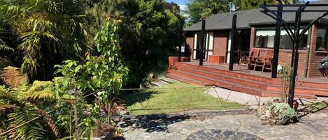 A house with a stone patio, a wooden deck, and a garden with various plants.