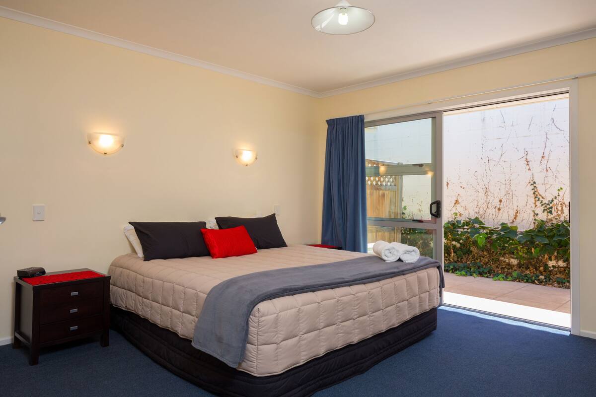 A bedroom with a bed, bedside table, and a view through a glass door to an outdoor area.