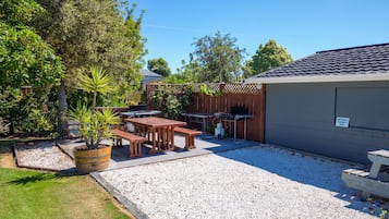 Een achtertuin met een barbecueplek, een picknicktafel en potplanten.