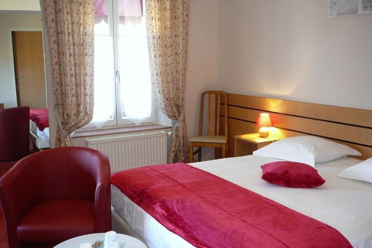 Una camera d'albergo con un letto, una sedia, un tavolo con una lampada e una finestra con tende.