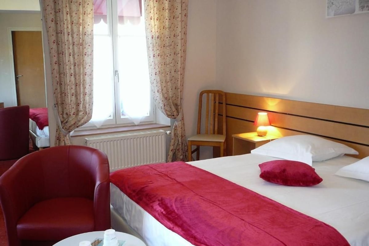 Una camera d'albergo con un letto, una sedia, un tavolo con una lampada e una finestra con tende.