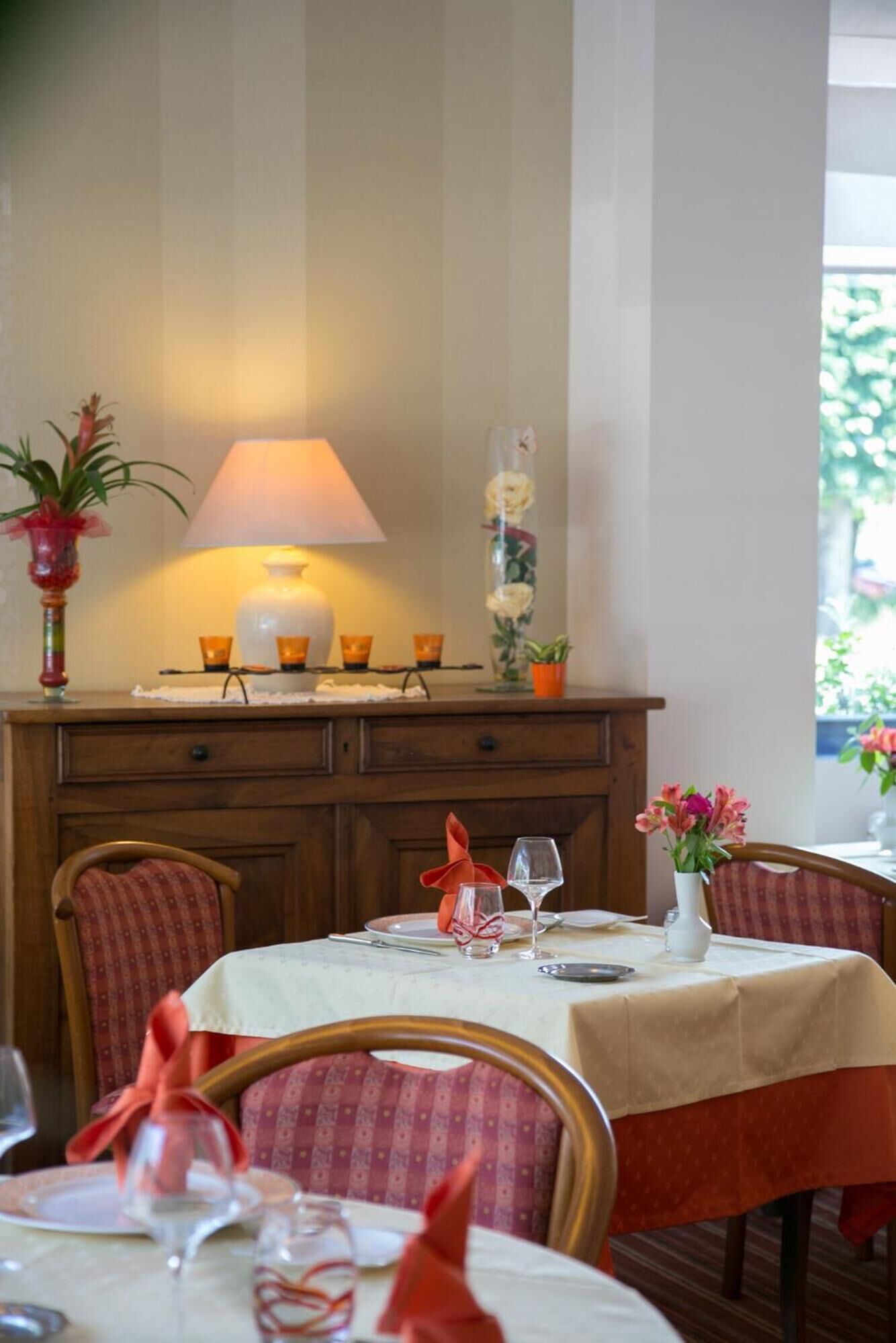 Un coin repas avec une table dressée pour deux personnes, une lampe et un vase décoratif orné de fleurs.