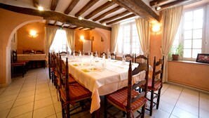 Ein Esszimmer mit einem langen Tisch, gedeckt für eine Mahlzeit, Holzsesseln und einer hohen Decke mit freiliegenden Balken.