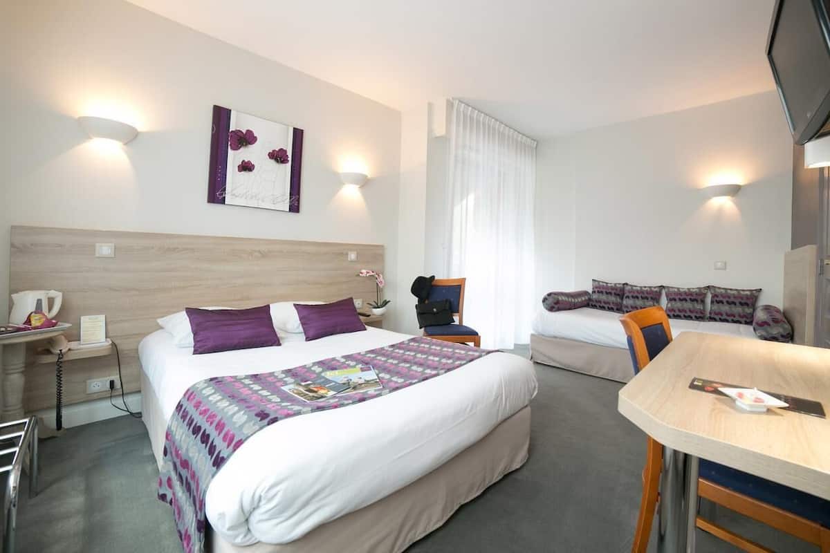 Une chambre d’hôtel comprenant un lit, une table de chevet, une chaise, un bureau et un téléviseur.