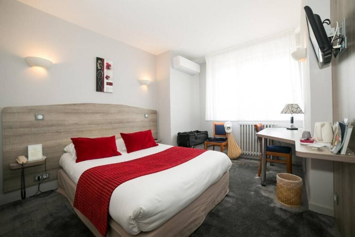 Ein Hotelzimmer mit Bett, Nachttisch, Lampe, Schreibtisch, Stuhl und Heizkörper.