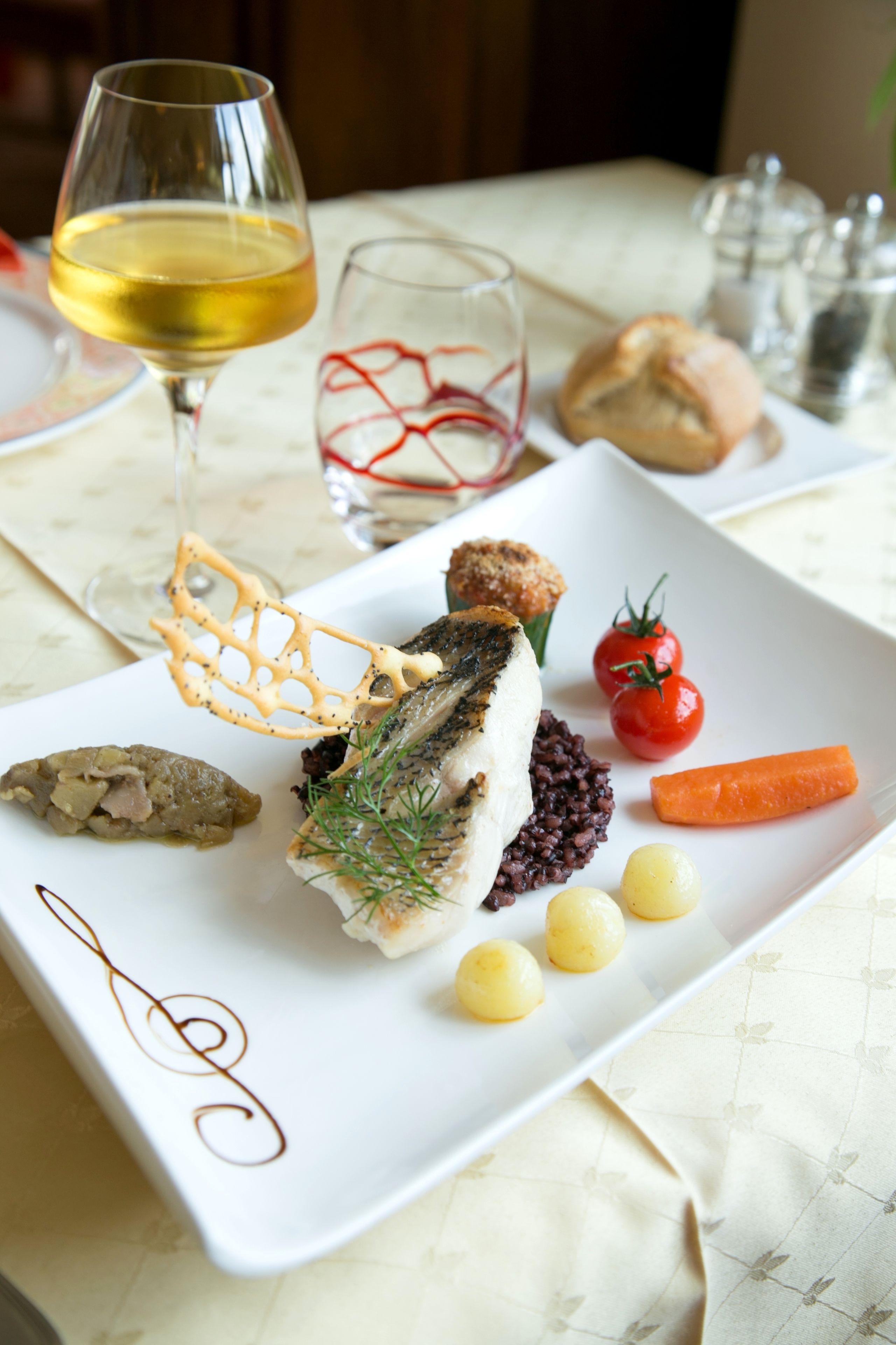 A white plate with a variety of food items including a piece of grilled fish, cherry tomatoes, a carrot, and some pickled vegetables.